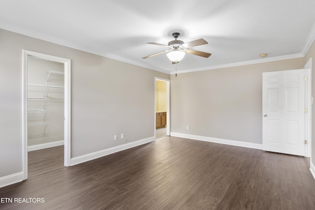 unfurnished bedroom featuring dark wood-style flooring, a closet, a spacious closet, ornamental molding, and baseboards