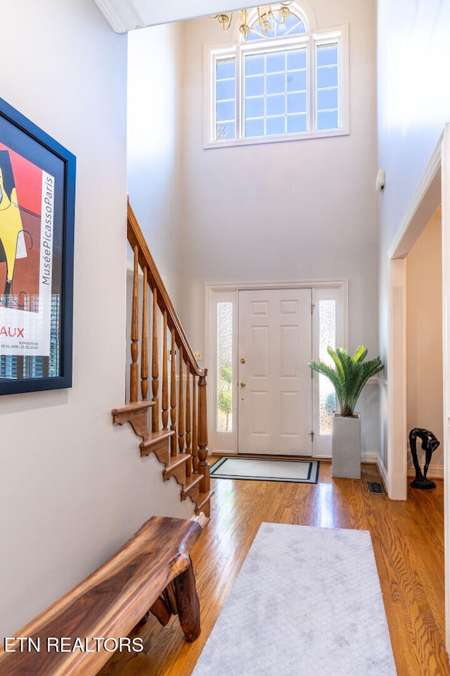 entrance foyer with stairway, a high ceiling, visible vents, and wood finished floors