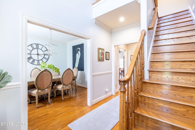 stairway with a notable chandelier, baseboards, wood finished floors, and crown molding