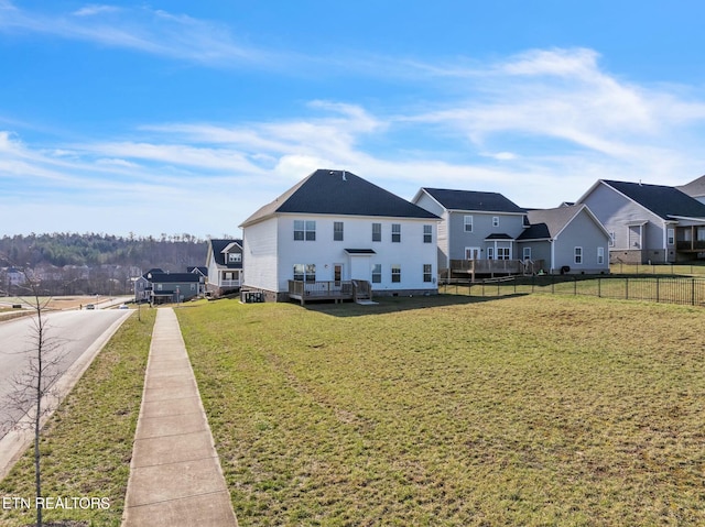rear view of house featuring a residential view, fence, a deck, and a lawn