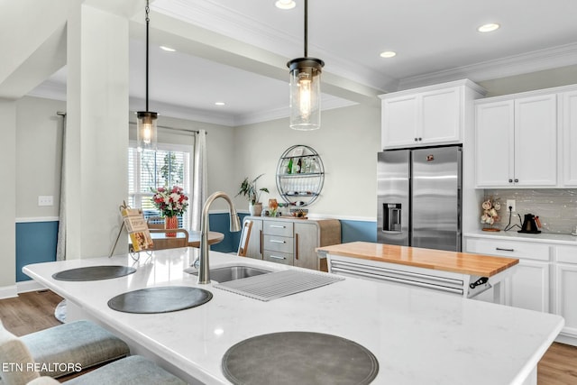 kitchen featuring crown molding, stainless steel refrigerator with ice dispenser, decorative backsplash, a sink, and wood finished floors