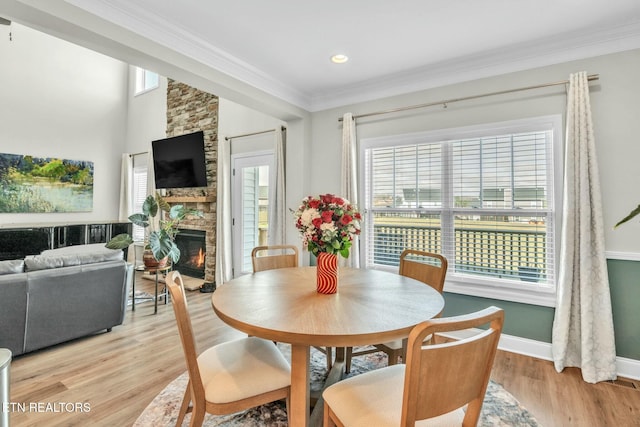 dining area featuring baseboards, light wood-style floors, a fireplace, and crown molding