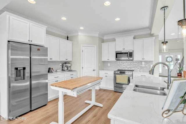 kitchen with ornamental molding, stainless steel appliances, light wood-style floors, white cabinetry, and a sink
