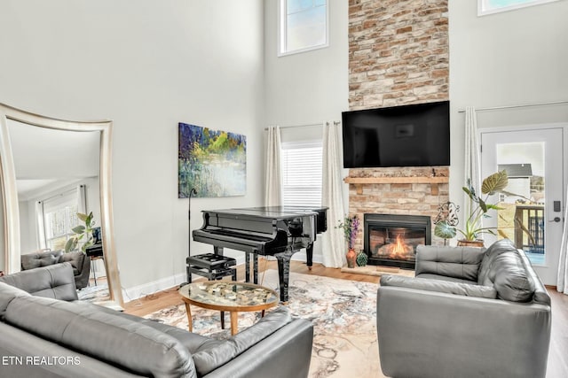 living room featuring a glass covered fireplace, baseboards, a high ceiling, and wood finished floors