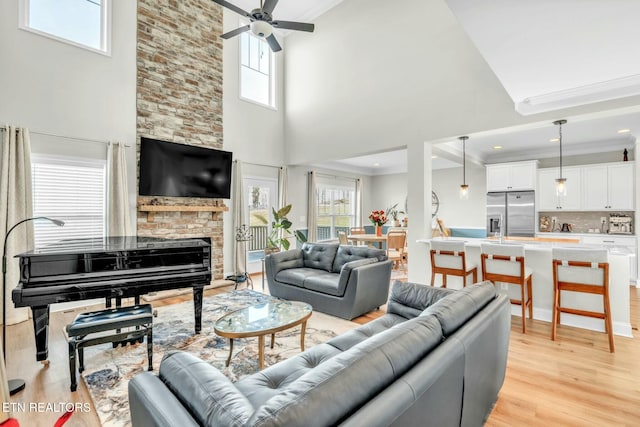 living room featuring light wood-style floors, crown molding, a stone fireplace, and ceiling fan