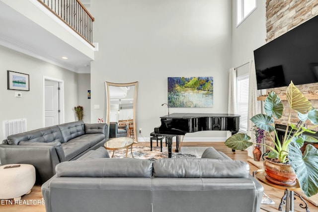 living area featuring a towering ceiling, visible vents, wood finished floors, and ornamental molding