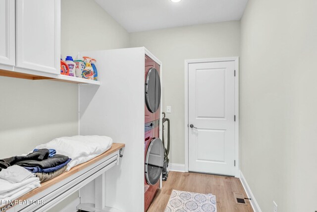 laundry area with stacked washer / dryer, visible vents, baseboards, light wood-style floors, and cabinet space
