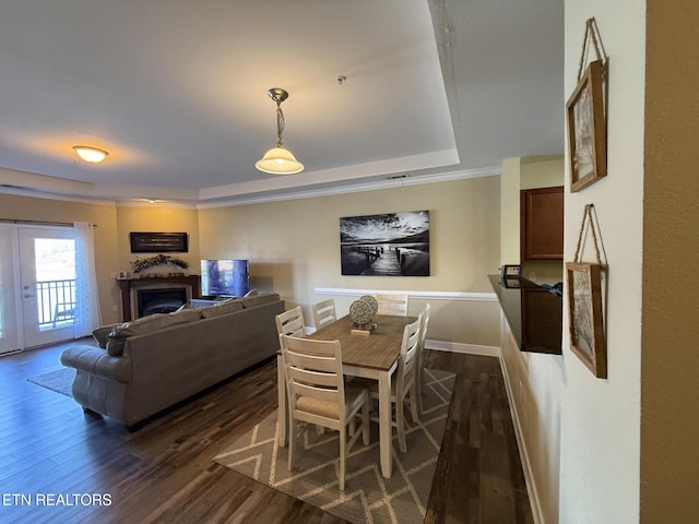 dining space featuring baseboards, dark wood-style floors, a tray ceiling, crown molding, and a fireplace