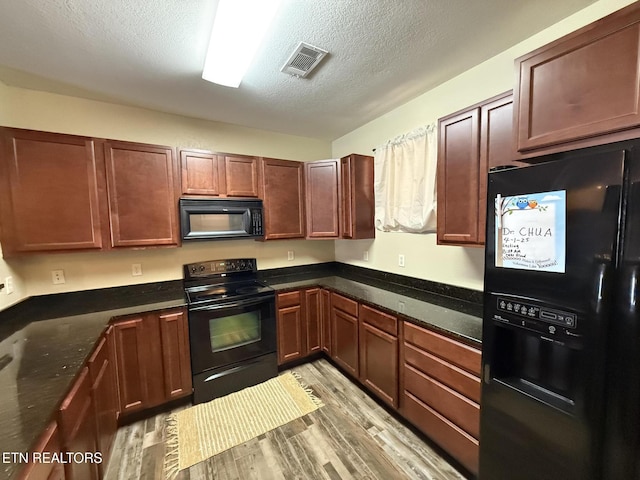 kitchen featuring light wood finished floors, visible vents, dark stone counters, a textured ceiling, and black appliances