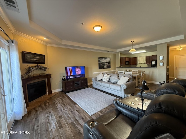 living room featuring a fireplace, a raised ceiling, visible vents, wood finished floors, and baseboards