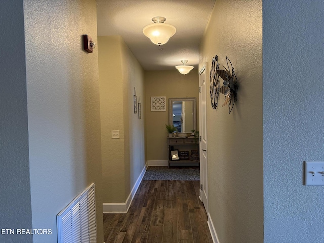 hallway featuring dark wood-style flooring, visible vents, and baseboards