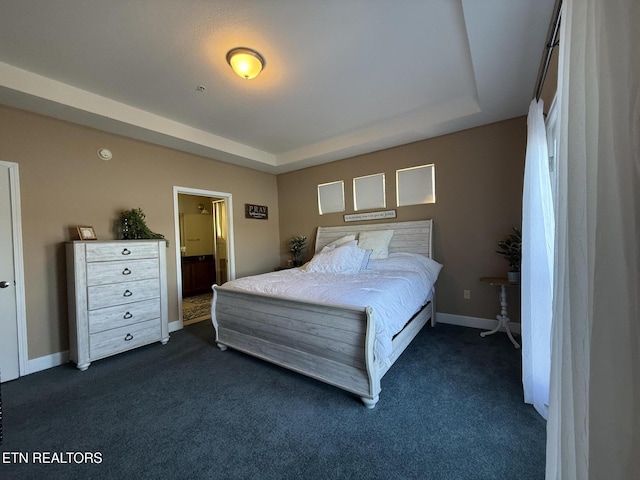 bedroom with ensuite bathroom, dark colored carpet, a tray ceiling, and baseboards