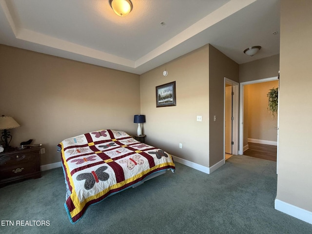 bedroom featuring a tray ceiling, dark carpet, and baseboards