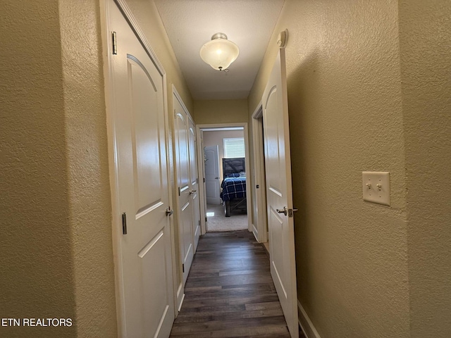 hallway with dark wood-type flooring and a textured wall