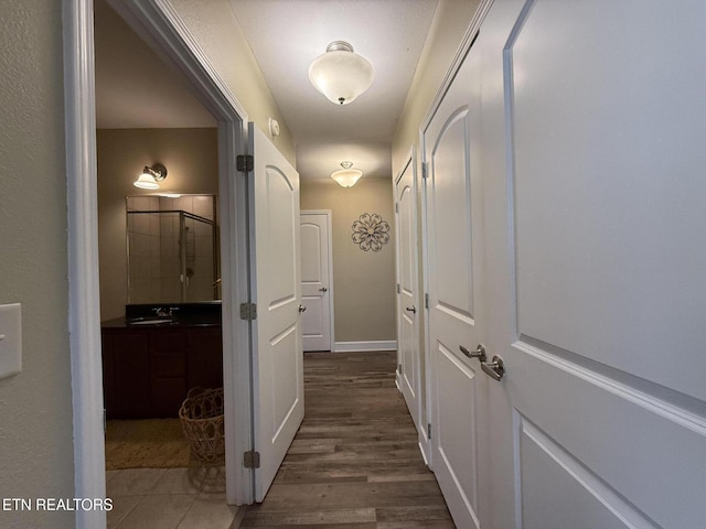 hallway with dark wood-style floors, baseboards, and a sink