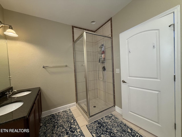 full bath with a stall shower, double vanity, a sink, and tile patterned floors