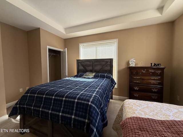 bedroom with light carpet, a tray ceiling, and baseboards