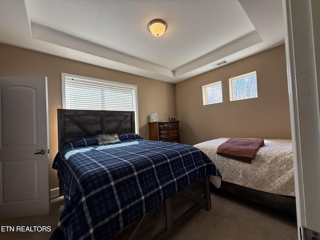 bedroom featuring visible vents, a tray ceiling, and carpet flooring