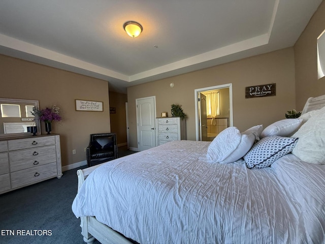 bedroom with connected bathroom, a raised ceiling, dark carpet, and baseboards