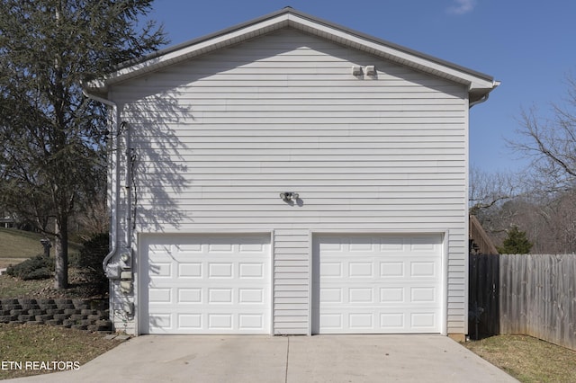 garage with concrete driveway and fence