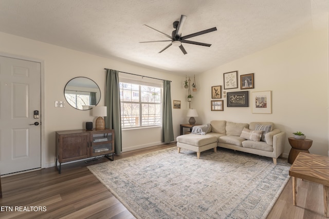 living room with a ceiling fan, wood finished floors, baseboards, vaulted ceiling, and a textured ceiling