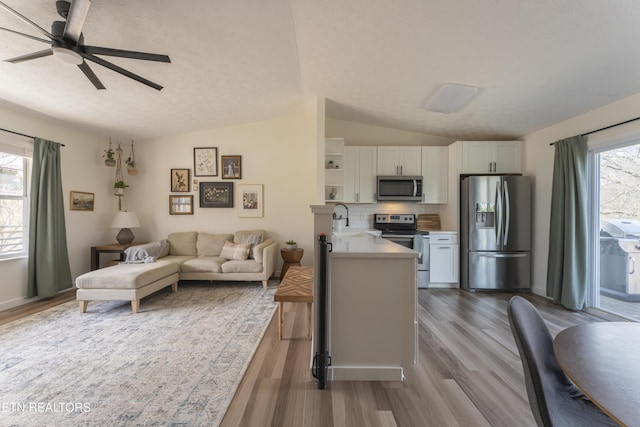 kitchen with a sink, white cabinetry, stainless steel appliances, light countertops, and lofted ceiling