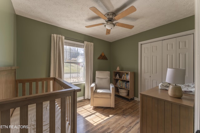 bedroom with a crib, a textured ceiling, a closet, light wood finished floors, and baseboards