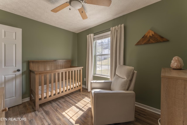 bedroom with a crib, wood finished floors, baseboards, and a textured ceiling