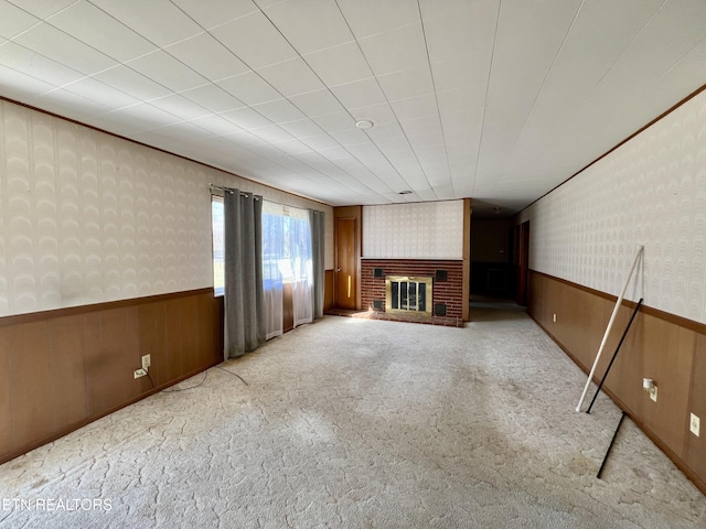 unfurnished living room with wallpapered walls, a brick fireplace, light colored carpet, and wainscoting