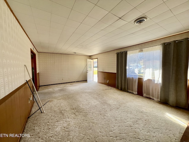 carpeted spare room featuring ornamental molding, a wainscoted wall, visible vents, and wallpapered walls