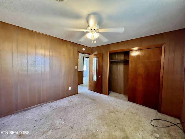 unfurnished bedroom with a closet, light carpet, wood walls, and ceiling fan