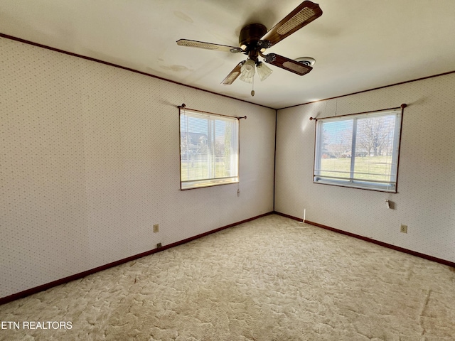 carpeted spare room featuring wallpapered walls, baseboards, a ceiling fan, and crown molding