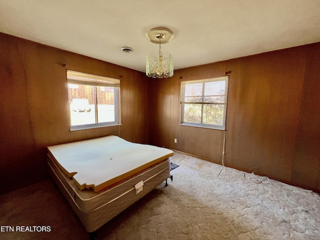 carpeted bedroom with wood walls, visible vents, and a chandelier