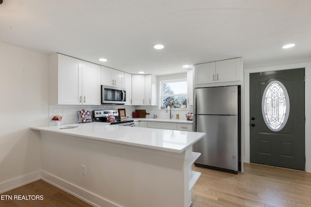 kitchen featuring a peninsula, light wood-style flooring, white cabinets, appliances with stainless steel finishes, and tasteful backsplash