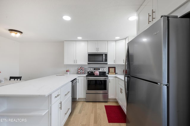 kitchen with decorative backsplash, light wood-style flooring, a peninsula, white cabinets, and stainless steel appliances