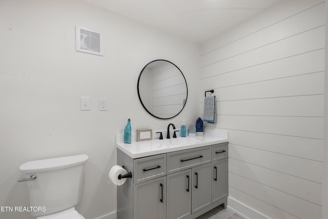 bathroom featuring visible vents, toilet, vanity, and wooden walls