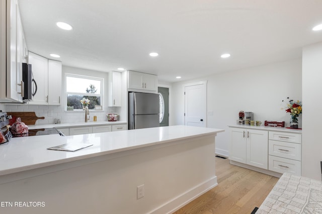 kitchen with light wood-style flooring, a sink, backsplash, stainless steel appliances, and light countertops