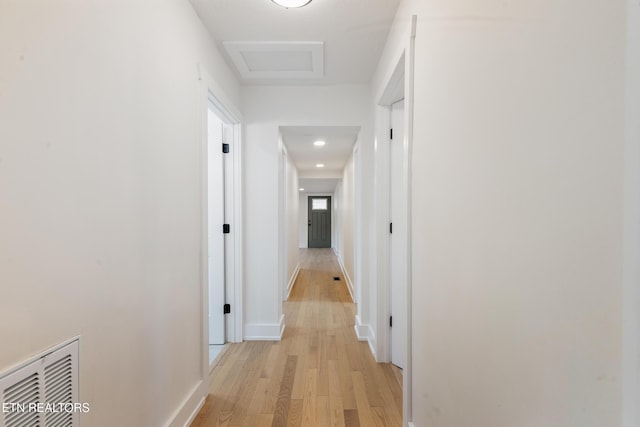 hallway with visible vents, baseboards, light wood-style floors, and attic access