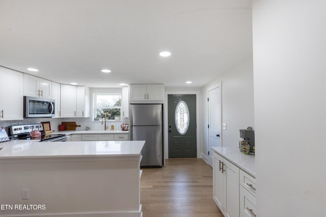 kitchen with light wood-type flooring, light countertops, white cabinets, appliances with stainless steel finishes, and tasteful backsplash