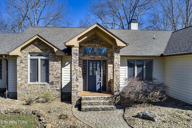 view of exterior entry featuring stone siding, a chimney, and roof with shingles