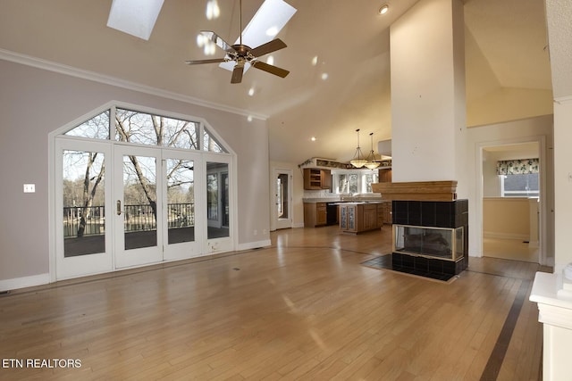 living room with high vaulted ceiling, a skylight, light wood-style floors, and plenty of natural light