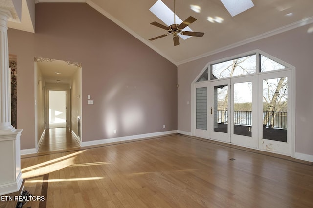 spare room featuring high vaulted ceiling, a skylight, wood finished floors, ornamental molding, and decorative columns