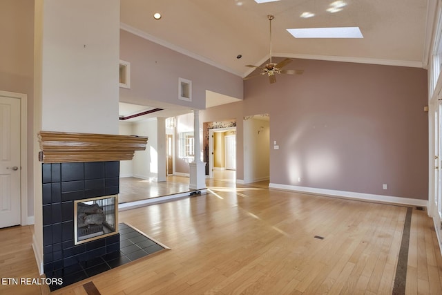 unfurnished living room with light wood-style floors, a skylight, ornamental molding, and a tile fireplace