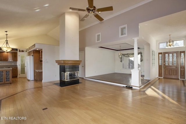 interior space featuring decorative columns, light wood-style floors, high vaulted ceiling, a tile fireplace, and ceiling fan with notable chandelier