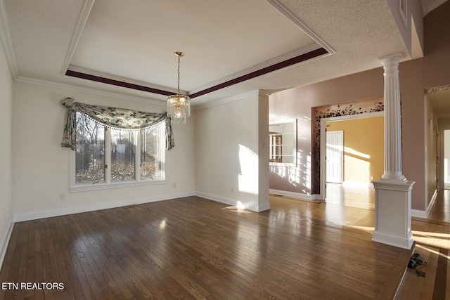 unfurnished dining area with a tray ceiling, crown molding, ornate columns, hardwood / wood-style floors, and baseboards