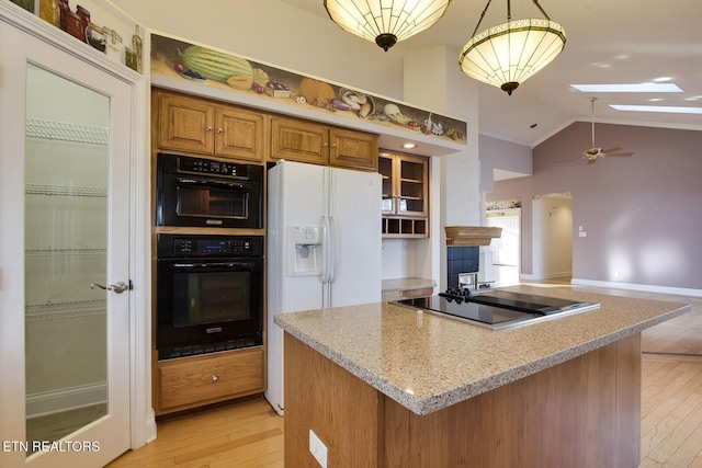 kitchen with black appliances, vaulted ceiling with skylight, brown cabinets, and light wood-style floors