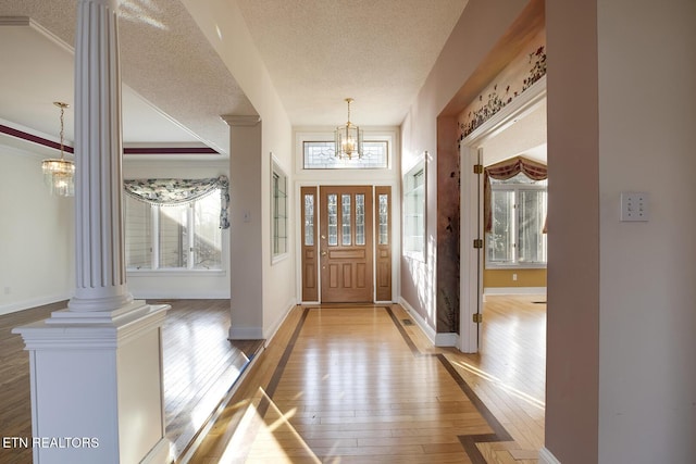 entryway with a notable chandelier, ornate columns, hardwood / wood-style floors, a textured ceiling, and baseboards