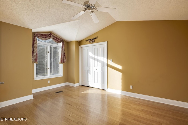 unfurnished bedroom with a closet, multiple windows, vaulted ceiling, and wood finished floors