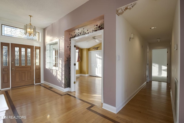 foyer with a notable chandelier, vaulted ceiling, light wood-type flooring, and baseboards