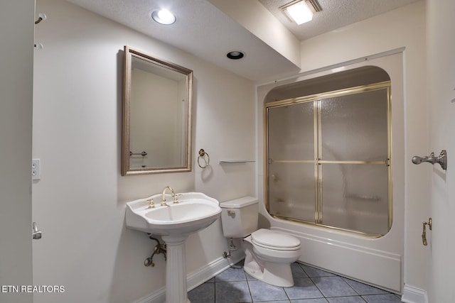 bathroom with baseboards, toilet, enclosed tub / shower combo, tile patterned floors, and a textured ceiling